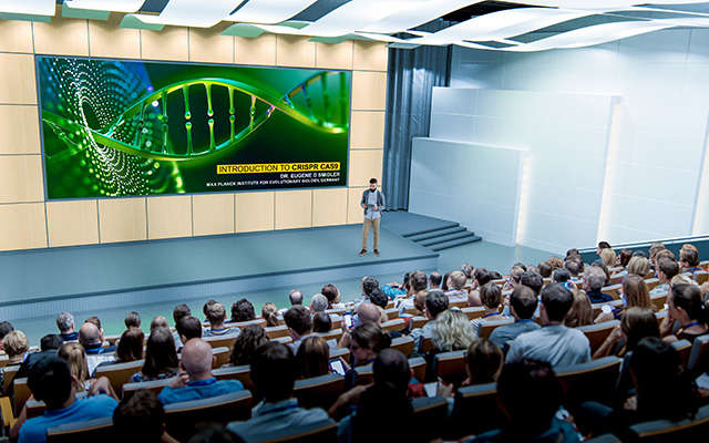 A presenter standing on stage in a lecture theatre full of people